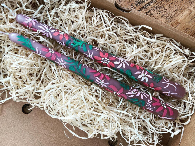 Two painted candles lying on a bed of shredded paper.